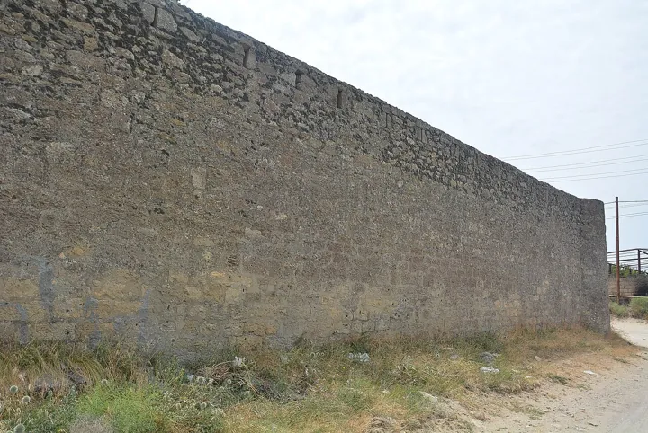 Photo d’origine : Haute muraille de pierre d'une enceinte fortifiée longeant un chemin.