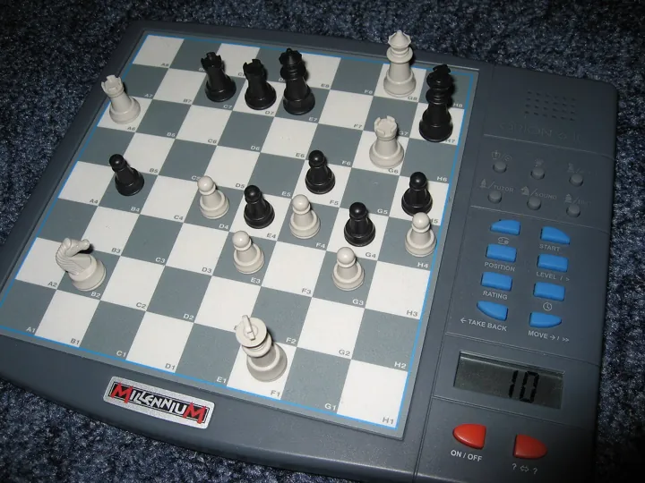 Photo d’origine : Un petit ordinateur d'échecs électronique en pleine partie, pièces blanches et noires sur l'échiquier.