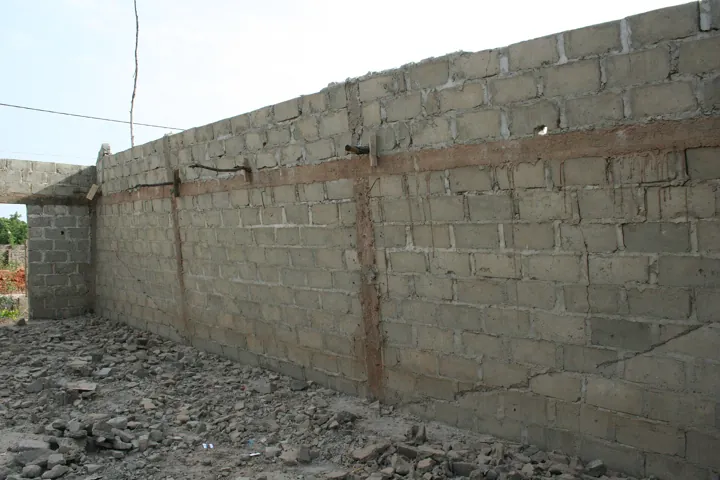 Photo d’origine : Un mur de parpaings inachevé, fissuré par les intempéries : un défaut de conception visible une fois l'ouvrage monté.