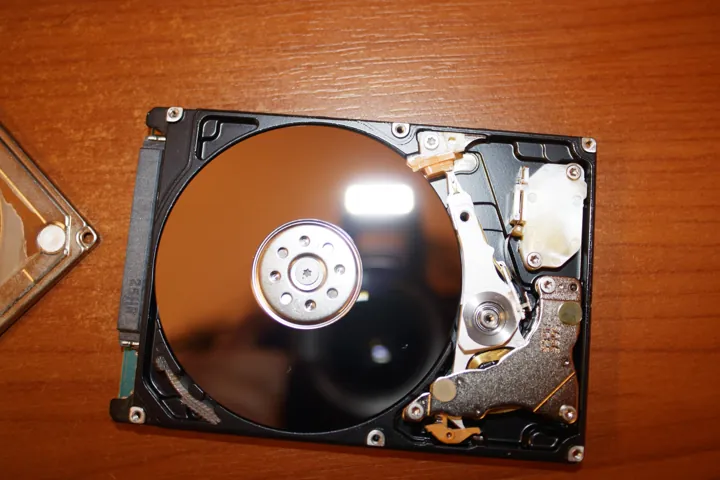 Photo d’origine : Un disque dur ouvert, plateau et bras de lecture visibles, posé sur une table de bois.
