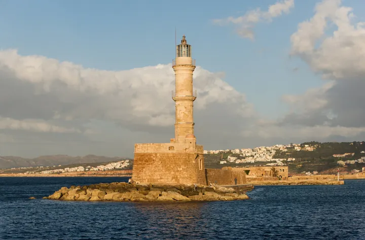 Original photo: Un phare de pierre sur une jetée rocheuse, éclairé par le soleil du soir au-dessus de la mer.