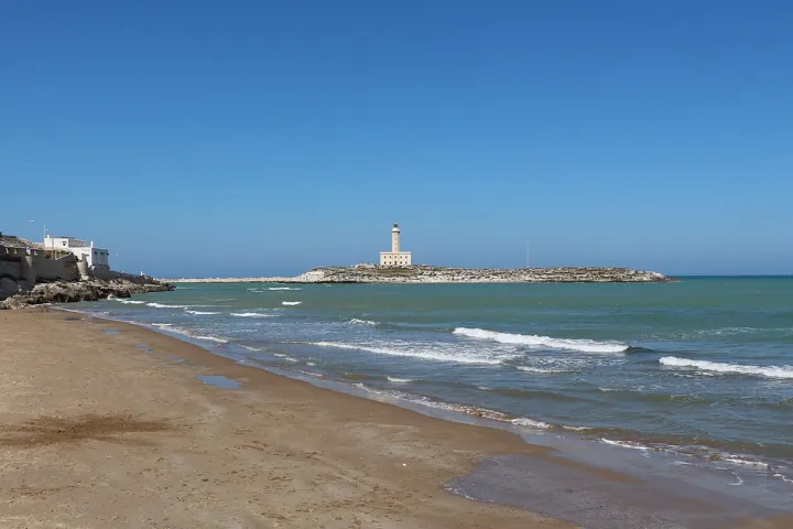 Original photo: Le phare de Vieste, sur son îlot, vu depuis la plage au bord d'une mer calme.