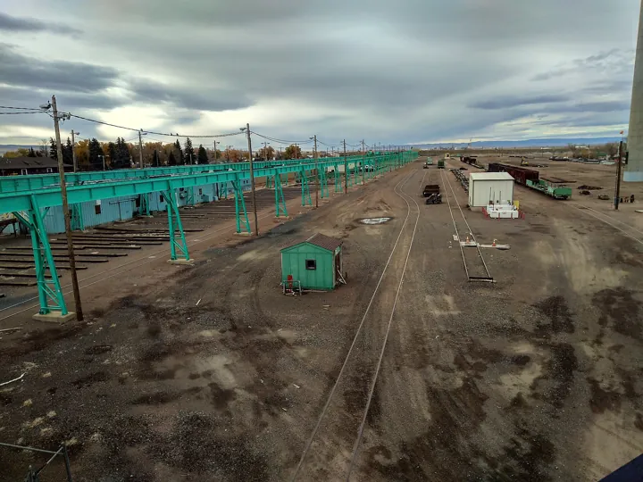 Photo d’origine : Vue plongeante sur un grand faisceau de voies et un atelier ferroviaire sous un ciel nuageux.