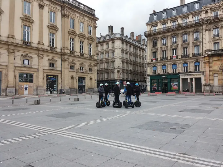 Original photo: Un petit groupe de touristes en gyropodes sur une place de Lyon, devant des immeubles anciens.