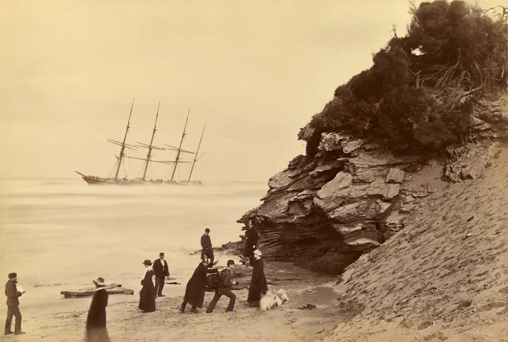 Original photo: Un grand voilier à quatre mâts échoué au large d'une plage, avec quelques promeneurs sur le sable.