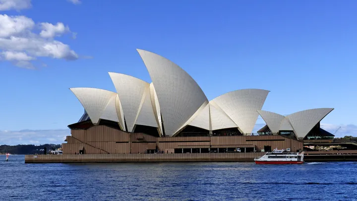 Photo d’origine : L'opéra de Sydney et ses coques blanches au bord de l'eau, sous un ciel bleu.
