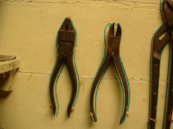 Original photo: Pinces accrochées à un mur d’atelier, chacune entourée du contour tracé de sa place.